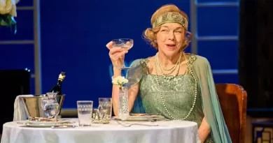 Actress Janie Dee in Art Deco clothing holds champagne glass at table.
